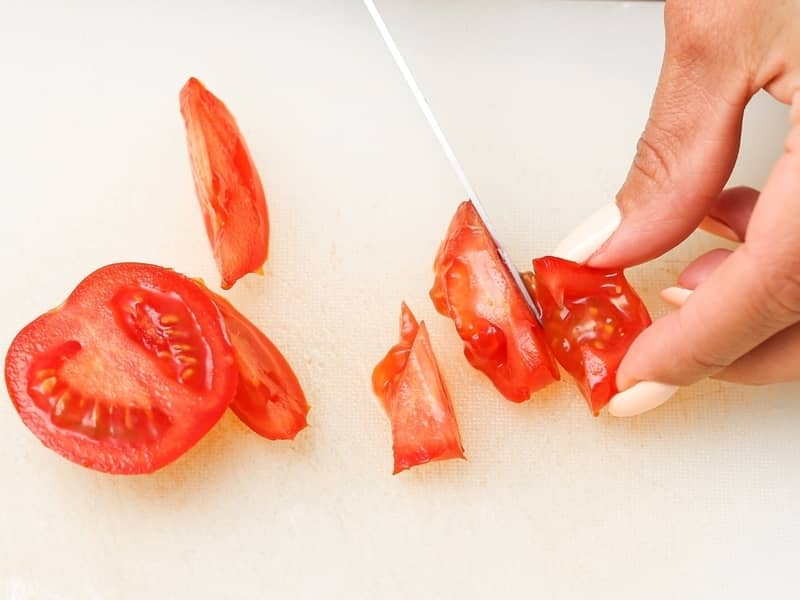 Hand cutting up a tomato to extract seeds